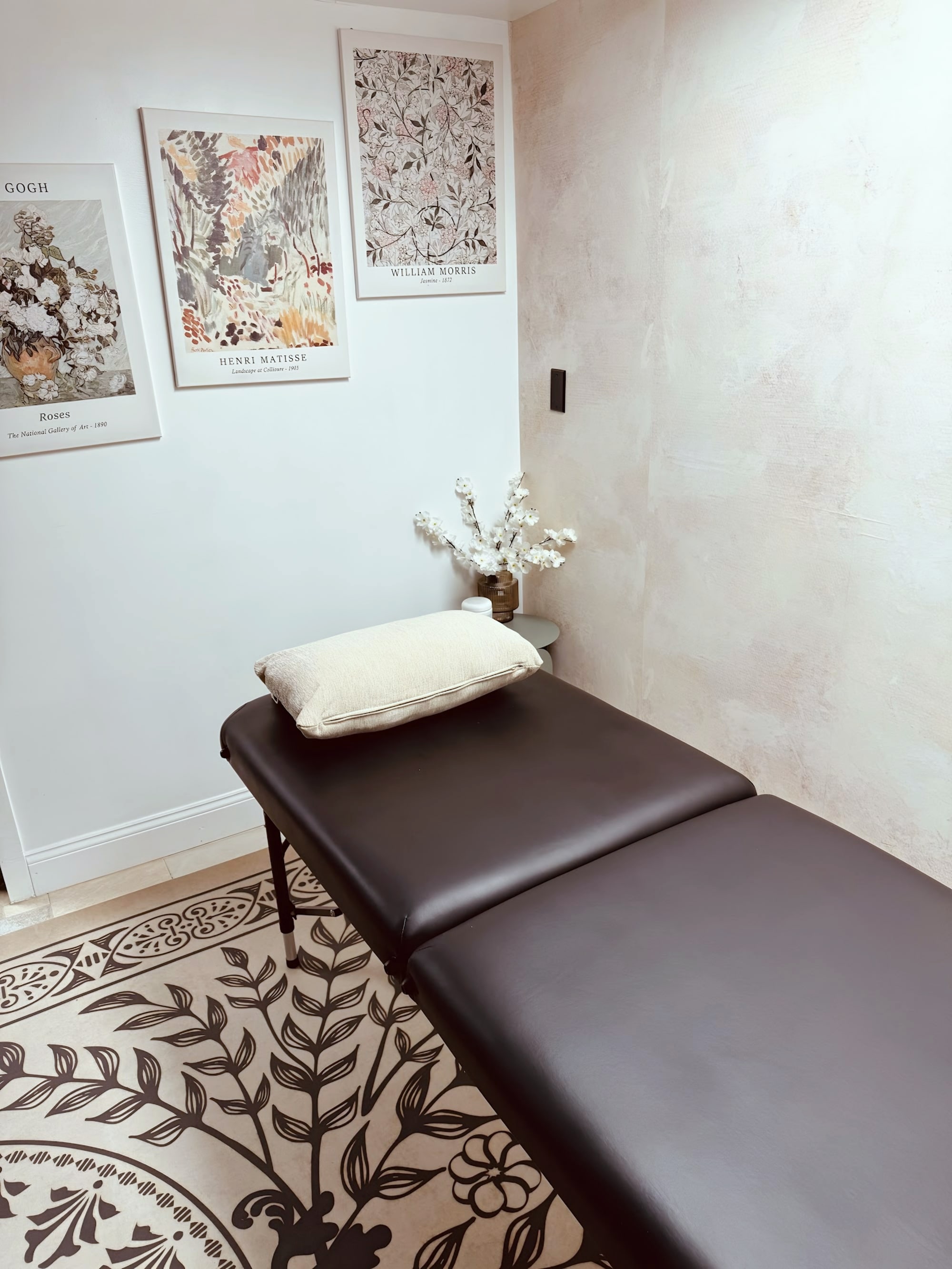 Treatment room with black massage table, pillow, and framed art prints